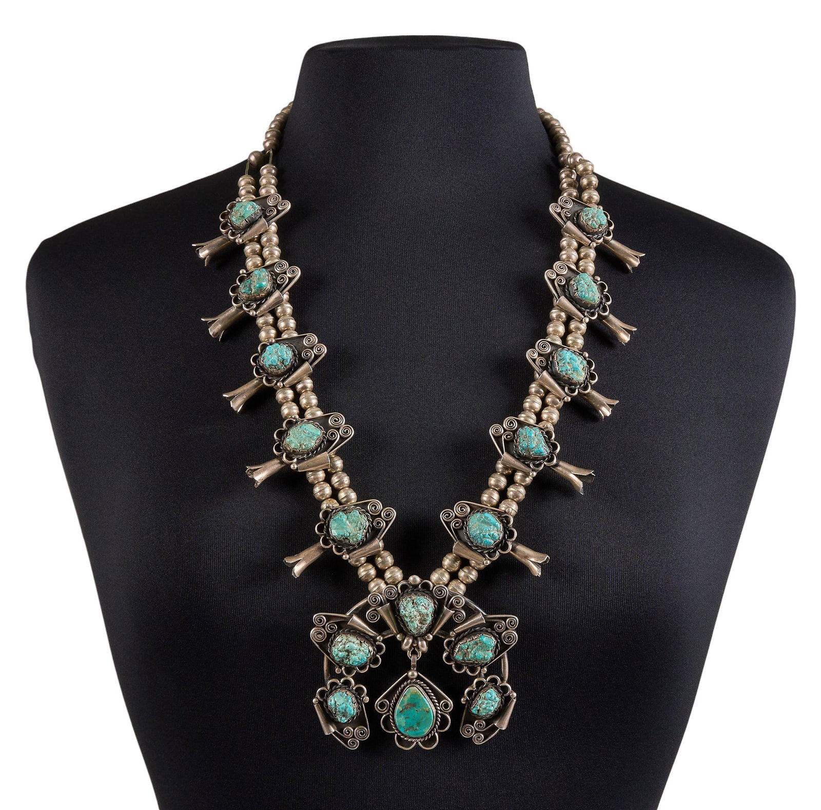 Navajo Sterling & Turquoise Squash Blossom: Navajo sterling silver squash blossom necklace, set with turquoise stones, featuring scrolled details and twisted wire motifs, with hook and eye closure Length: 28 in. Total weight: 272.0 g Provenance
