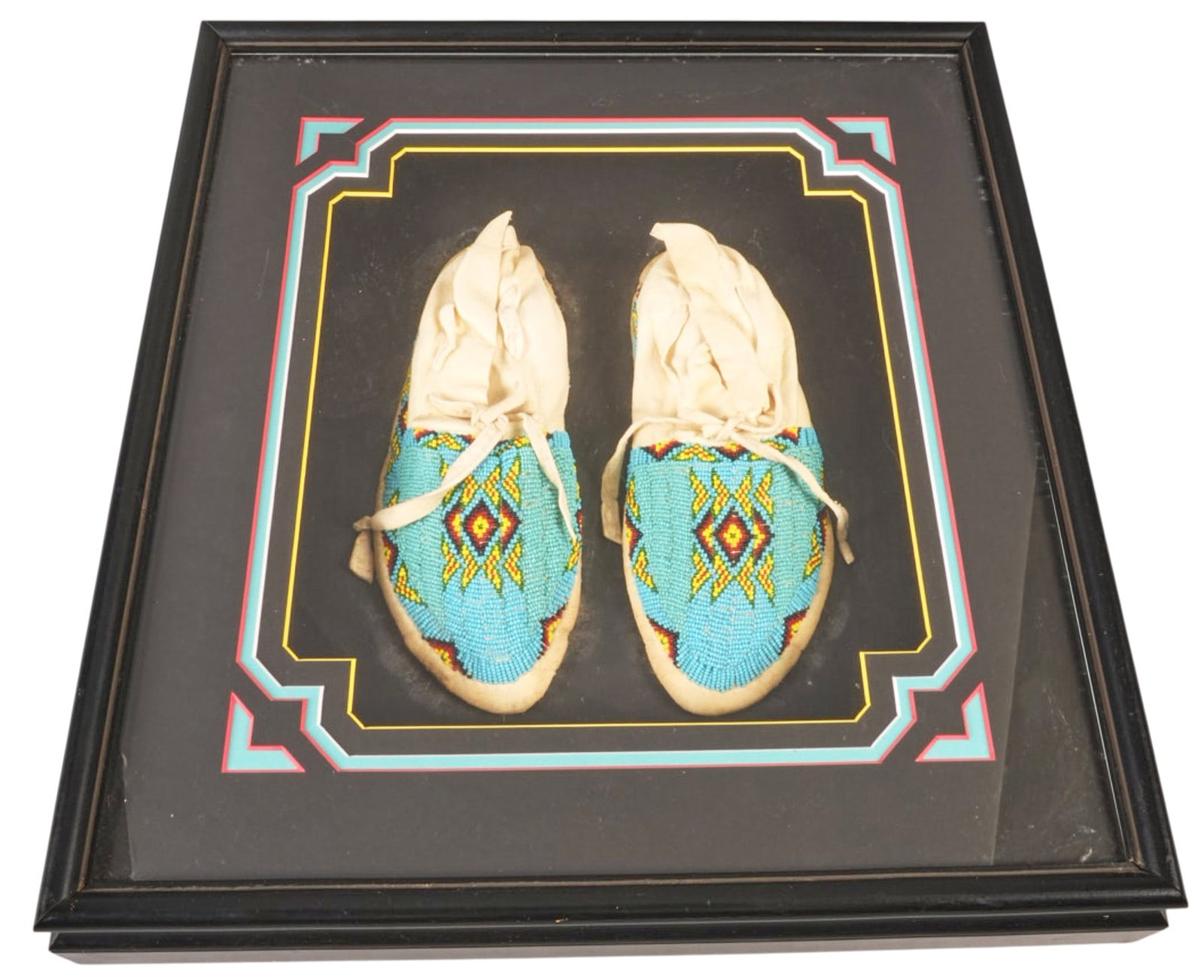 Beaded Moccasins in Shadowbox Frame: Framed pair of Native American style with geometric design height 20 in. x width 19 in. x depth 3.5 / frame Provenance: Property from a home in San Antonio, Texas