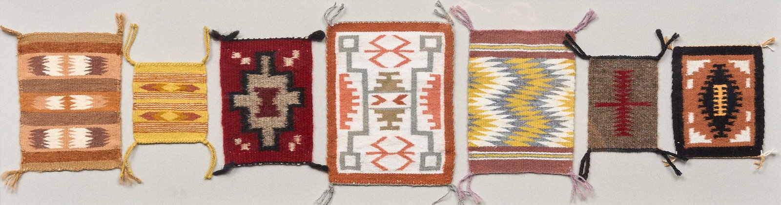 (7) Navajo Miniature Rugs: (7) Navajo miniature rugs, The Squash Blossom (Colorado Springs, Colorado) gallery label on the verso sight: 31 x 9 in., frame: 35 x 13 in. Provenance: Property from a Florissant,