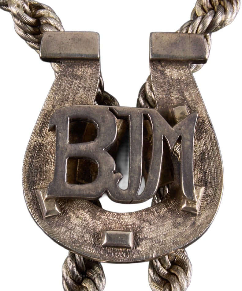 Red McCombs | Sterling Silver BJM Bolo Tie: Sterling silver horseshoe motif bolo tie with monogrammed "BJM" to slide, on fancy rope chain with twisted aiguilettes Total weight: 137.3 g Provenance: Property from the per