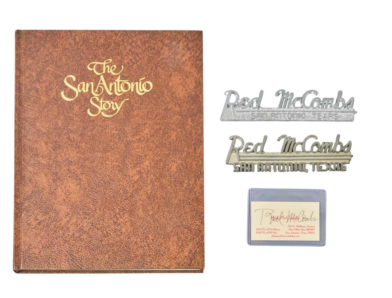 Red McCombs | Group of Vintage McCombs Items: Red McCombs signed business card, signed 'The San Antonio Story' book, two Red McCombs dealer emblems height 12.5 in. x width 10 in. x depth 5 in. / book Provenance: Property from the