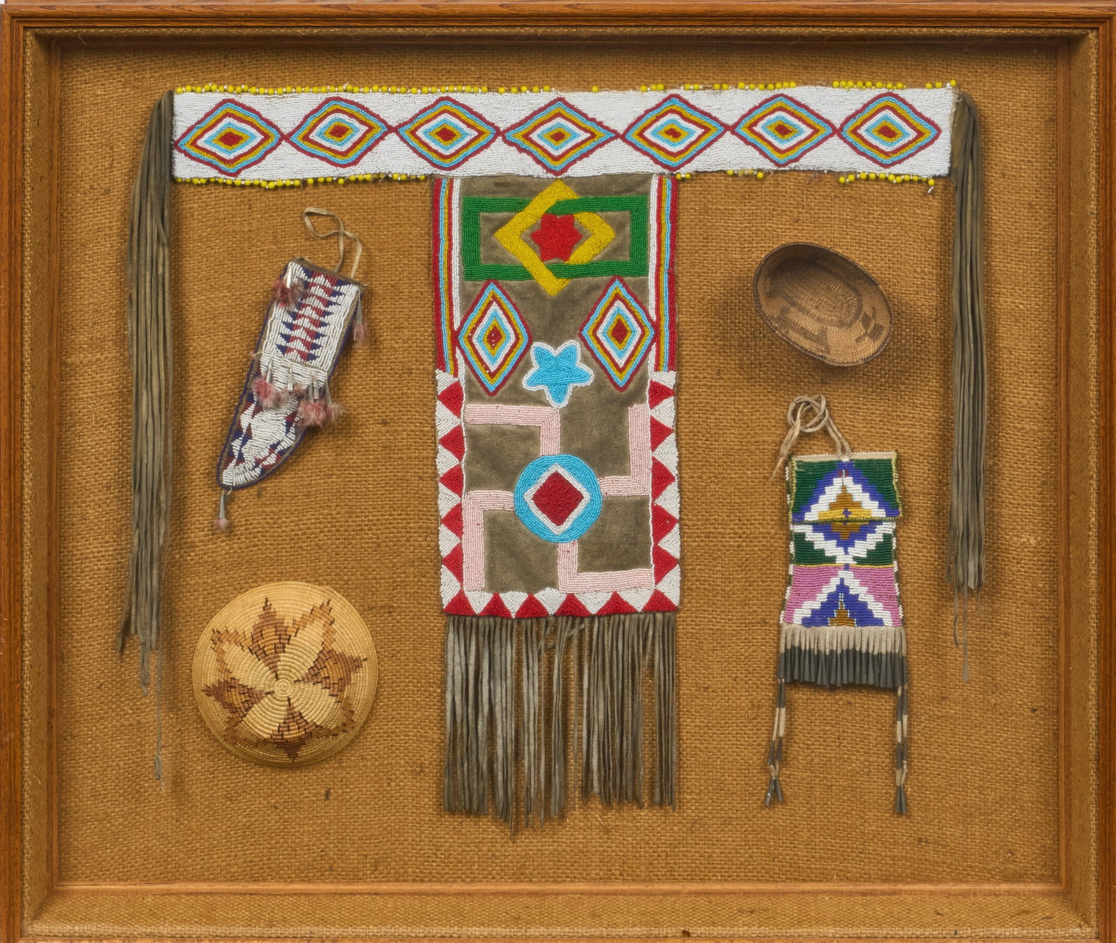 Red McCombs | Framed Collection of Native American Items: Framed collection of Native American items, includes two baskets, a beaded knife sheath, a beaded purse, and beaded T-shaped article of clothing height 34 in. x width 39 in. x depth 3 in. Proven