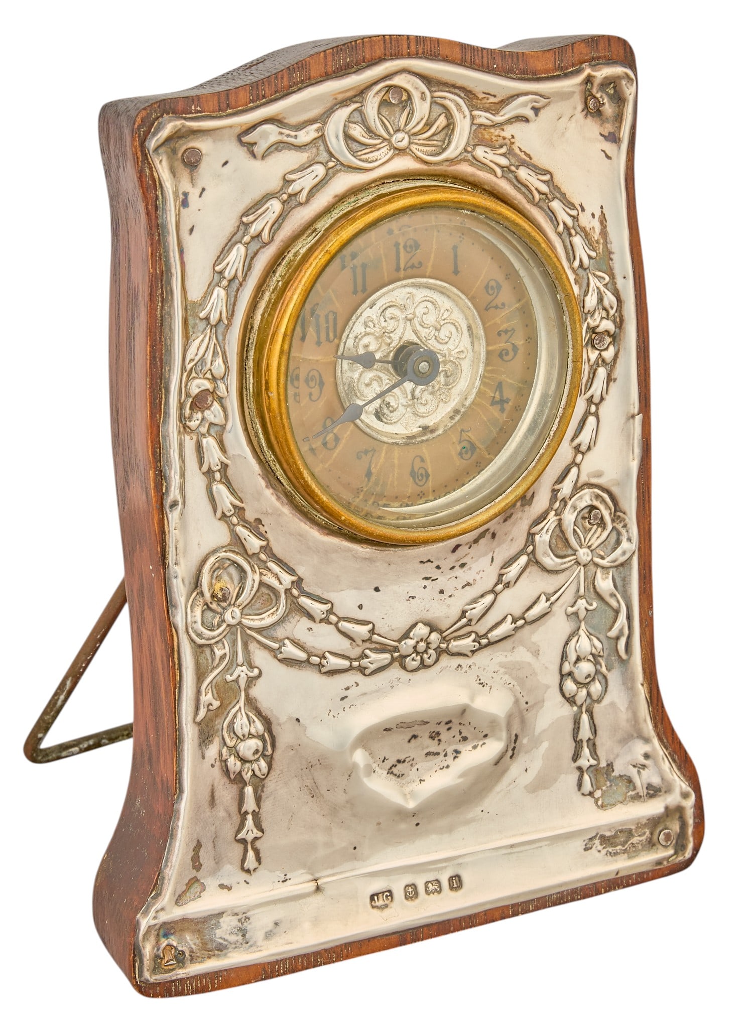 Red McCombs | Edwardian Sterling Silver Easel Clock: English Edwardian sterling silver-mounted easel clock, Birmingham, 1908, shaped mahogany case mounted with embossed silver front decorated with ribbon-tied floral garlands, circular Arabic numeral