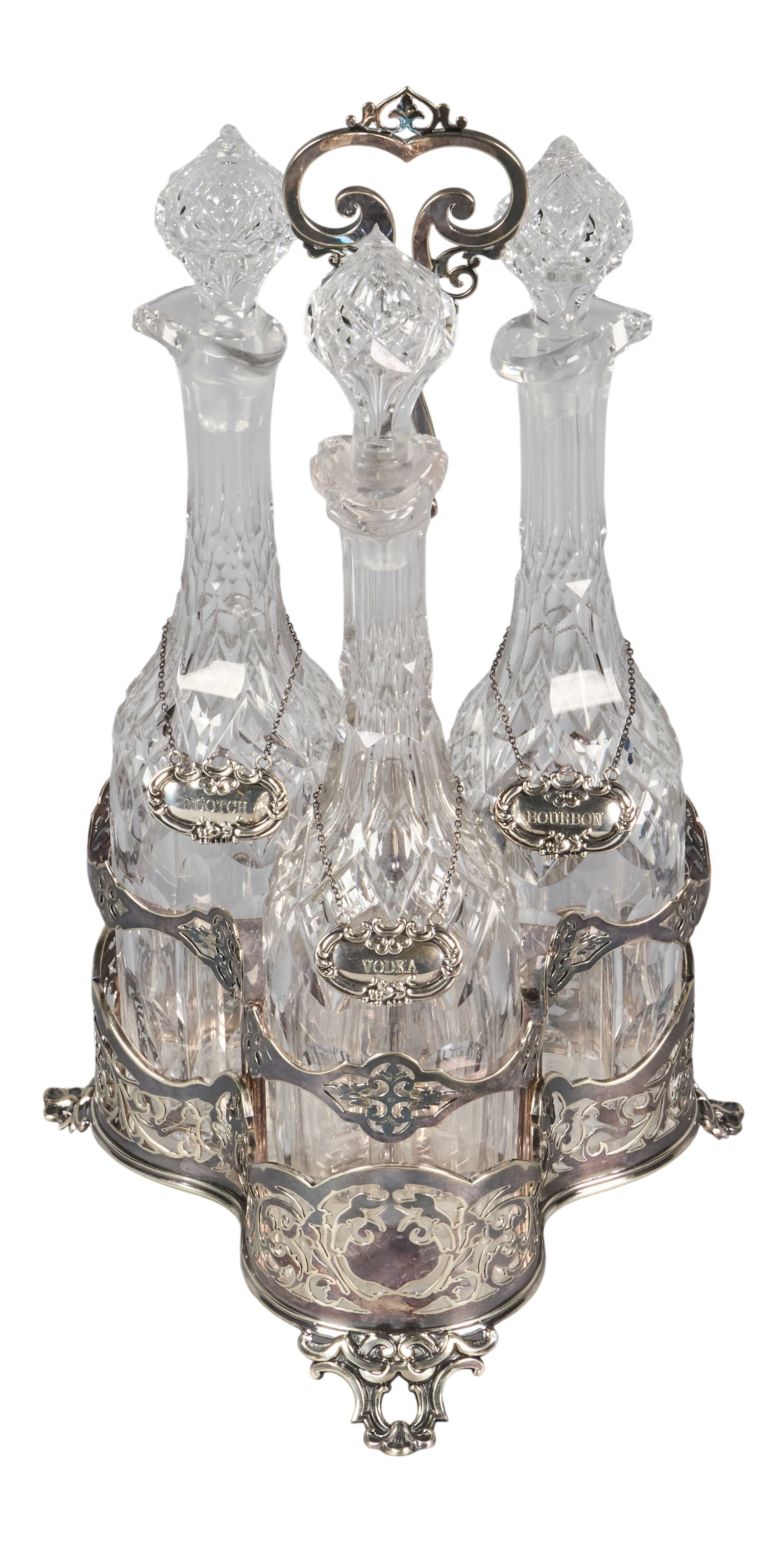 Red McCombs | English Silverplate Cut Crystal Tantalus: English silverplate tantalus, late 19th/early 20th century, fitted with three cut crystal decanters with faceted stoppers, each with sterling silver hanging spirit label, set within pierced 