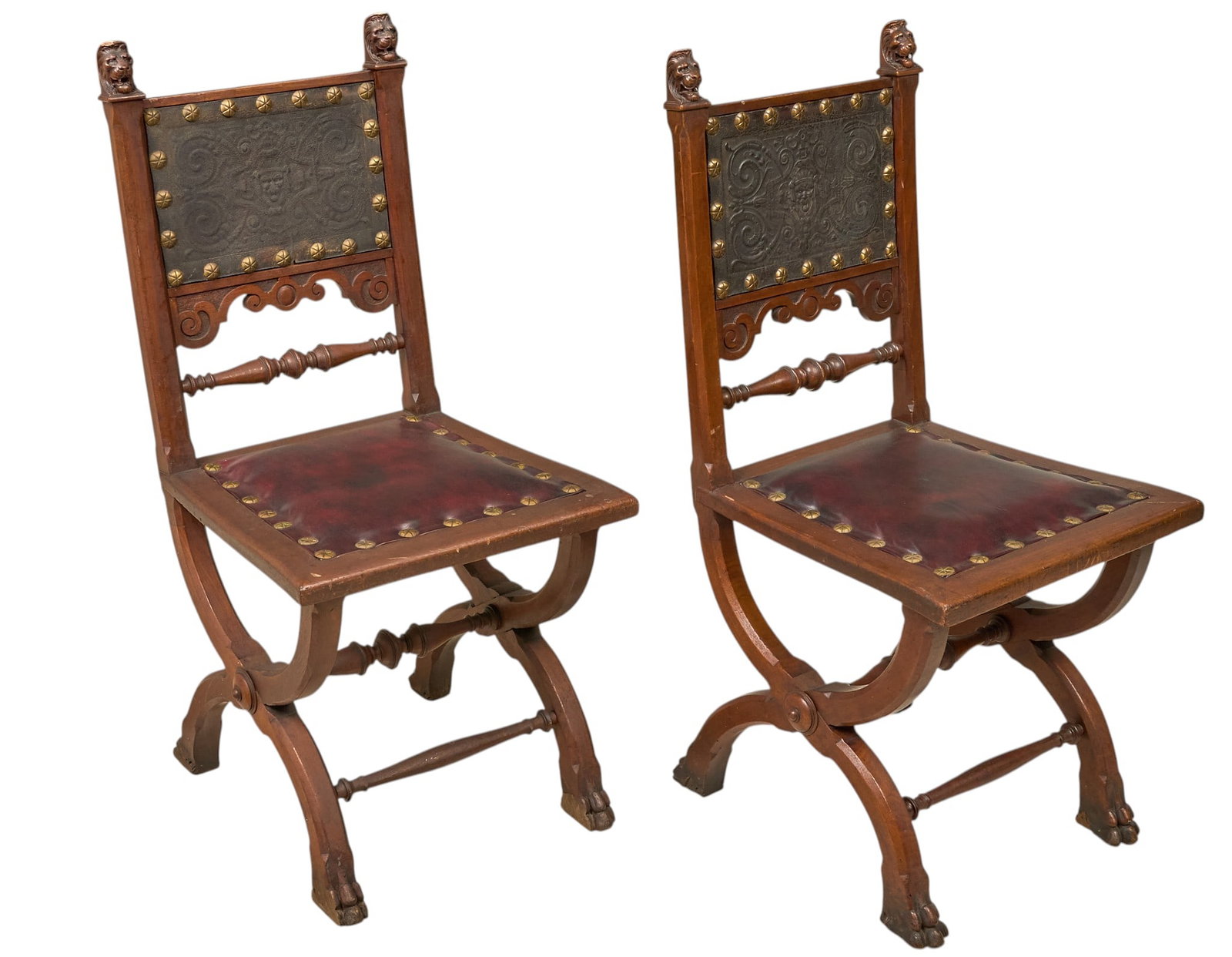 Red McCombs | Pair of Gothic Chairs: Matched pair of continental Gothic Revival carved side chairs, each with carved lion mask finials, embossed leather back with brass bosses, scrolled supports with paw feet height 38 in. x width 