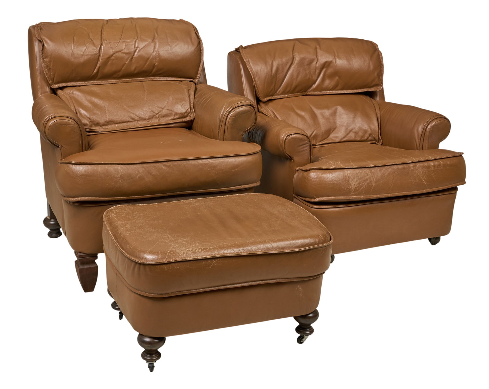Red McCombs | Pair of Leather Lounge Chairs with Ottoman: Pair of brown leather lounge chairs supported on turned feet, with ottoman supported on bun feet with rolling wheels, original makers tag on underside height 38 in. x width 36 in. x depth 37 in. / lar