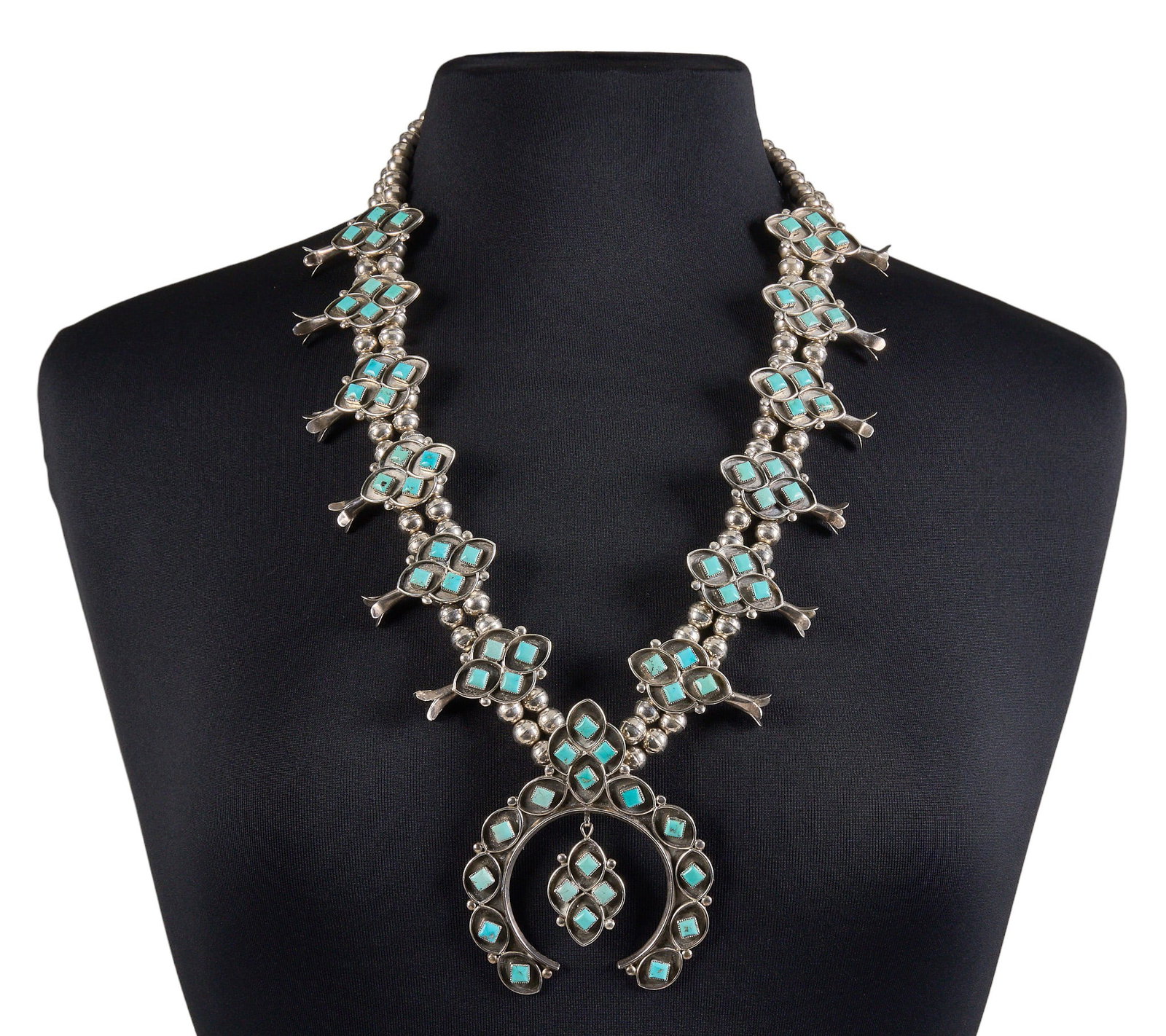 Sterling & Turquoise Squash Blossom: Sterling silver squash blossom necklace set with square turquoise cabochons in cluster design, with hook and eye closure Length: 27 in. Total weight: 206.3 g Provenance: Property from a home in S