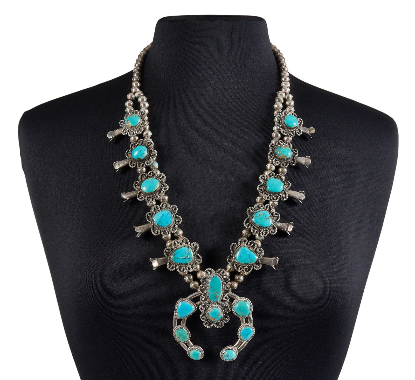 Sterling & Turquoise Squash Blossom: Sterling silver squash blossom necklace set with turquoise cabochons, featuring twisted wire motifs in floral design, marked "F-77" Length: 28 in. Total weight: 216.1 g Provenance: Prop