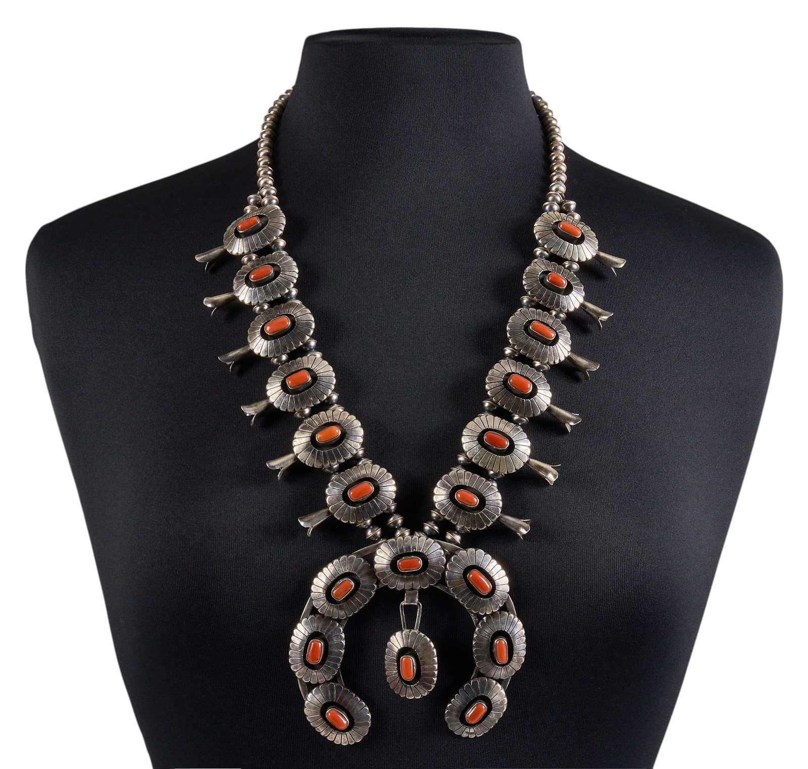 Sterling & Coral Shadowbox Squash Blossom: Sterling silver squash blossom necklace set with coral cabochons in shadowbox style settings, with large naja and hook and eye closure, marked to naja's reverse Length: 26 in. Naja: 3.75 in. 