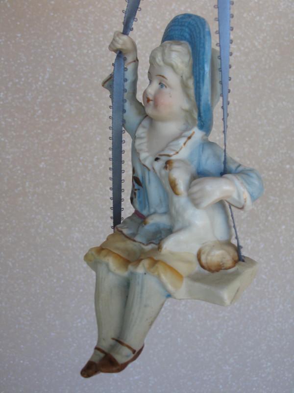 All-bisque German "Swinger" c1890-00s 6" (15cm) .: All-bisque German "Swinger" c1890-00s 6" (15cm) . Painted features, wide brim blue hat, blue-tan outfit with hand painted flower, also holding a molded puppy while seated on her swing seat and holding