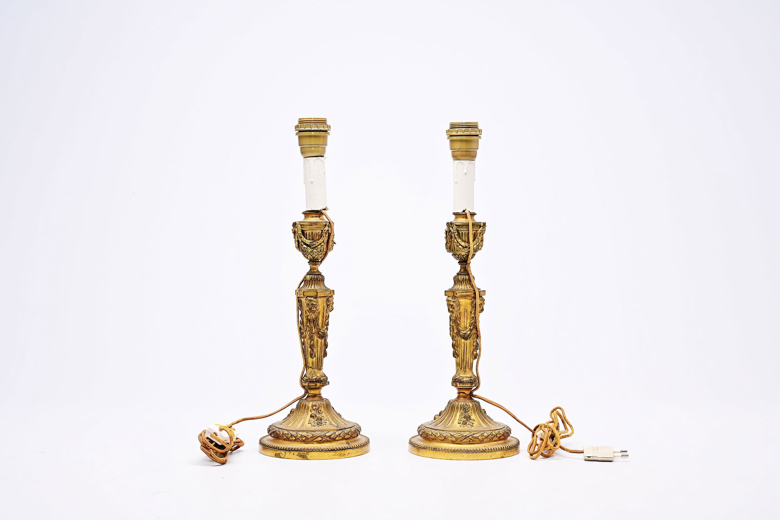 A pair of French Neoclassical gilt bronze candlesticks with lion heads and garlands mounted as: A pair of French Neoclassical gilt bronze candlesticks with lion heads and garlands mounted as lamps, 19th C. H 44,3 cm