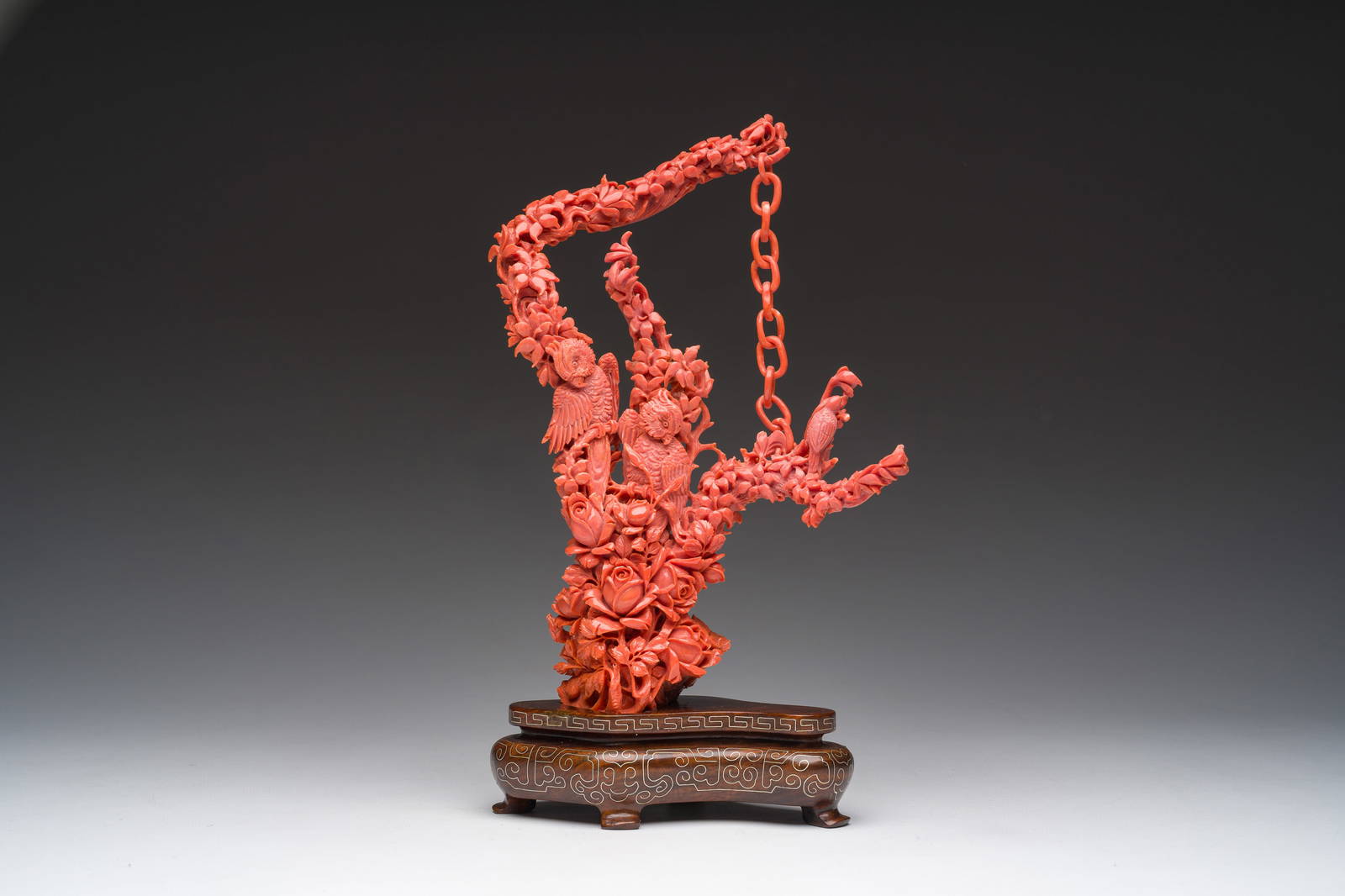 A Chinese red coral group of parrots among blossoming branches on a silver-inlaid wooden stand,