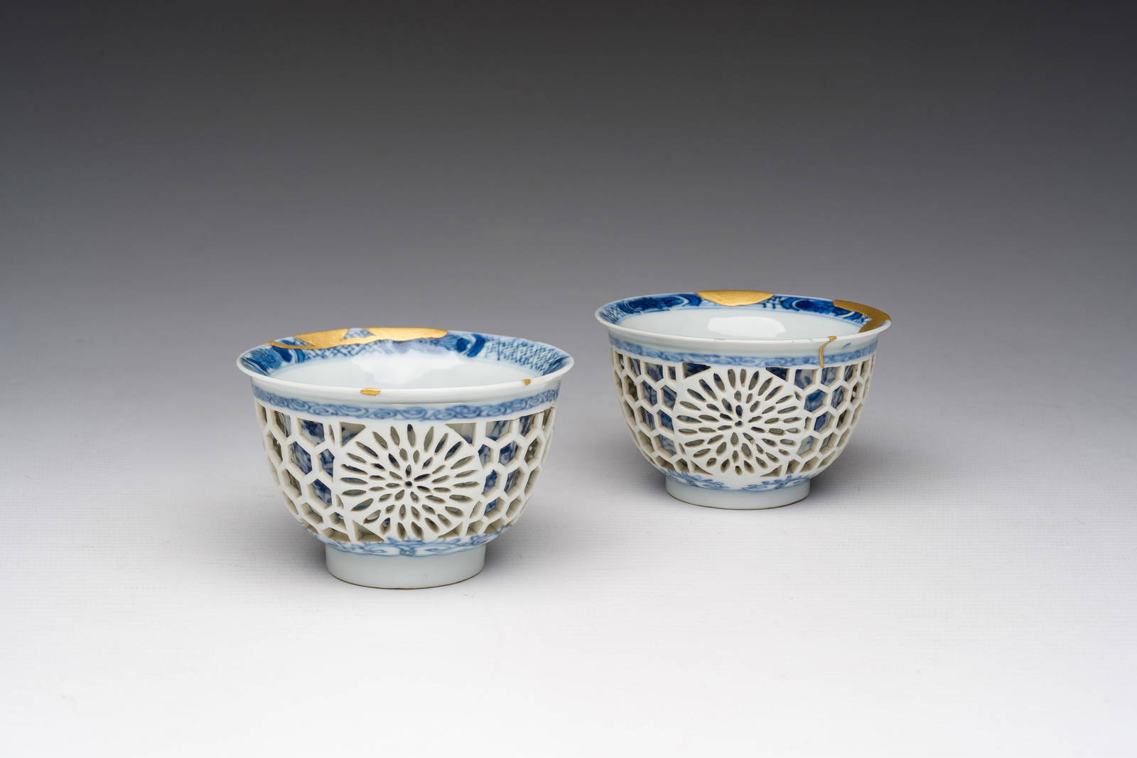 A pair of Chinese blue and white reticulated double walled cups with floral design and kintsugi