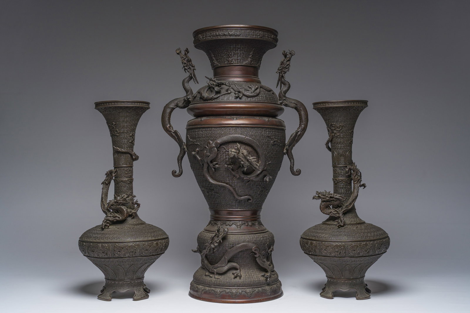 A Japanese three-piece bronze garniture with dragon relief design, Meiji, 19th C.: A Japanese three-piece bronze garniture with dragon relief design, Meiji, 19th C. H 69,5 - 50,5 cm