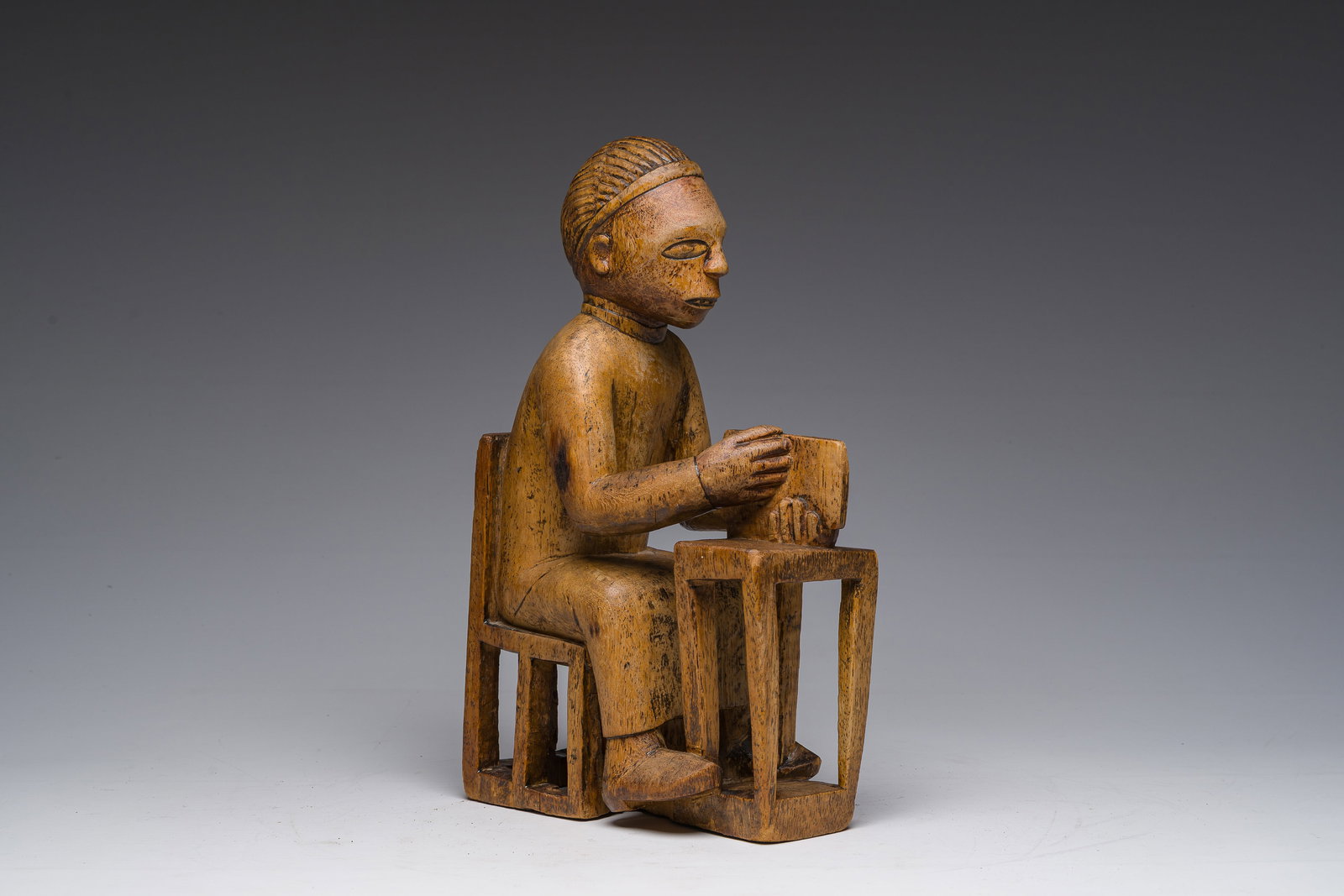 A Congolese Bakongo wooden sculpture of a seated man at a desk with a book in his hand, first third (1 of 8)