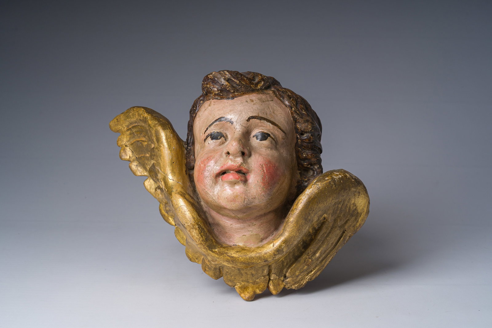 A gilt and polychrome decorated wooden angel's head, 18th C. (1 of 2)