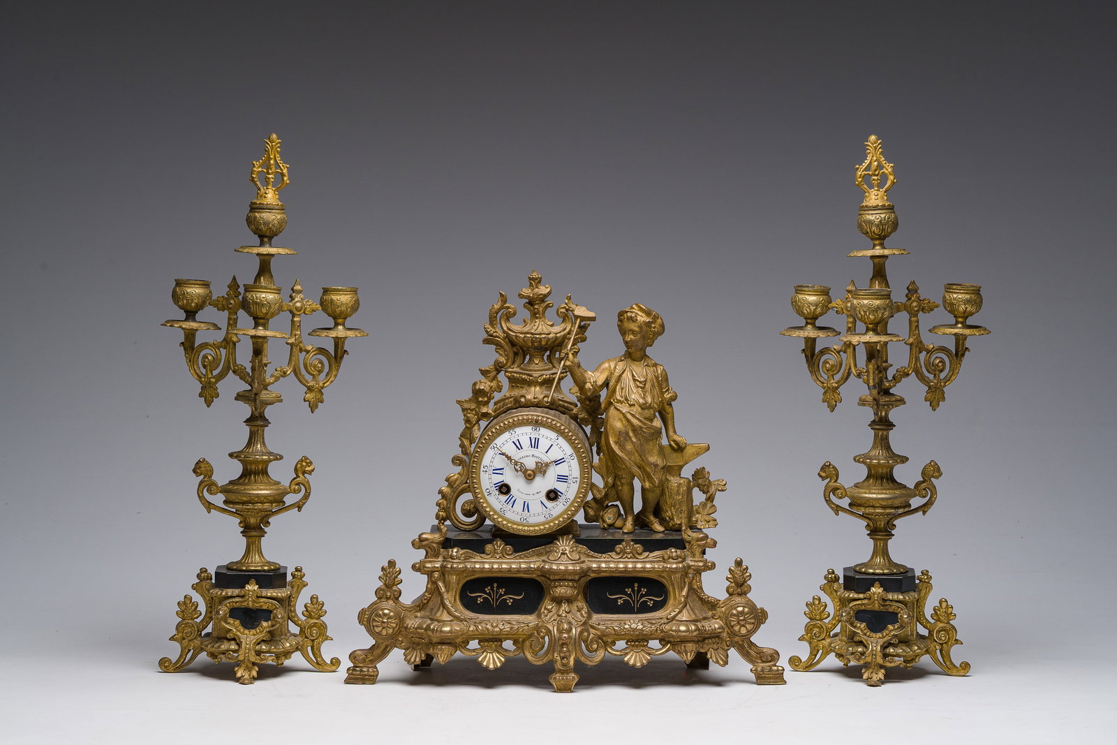 A French gilt bronze and black marble three-piece clock garniture crowned with a metalworker, (1 of 12)