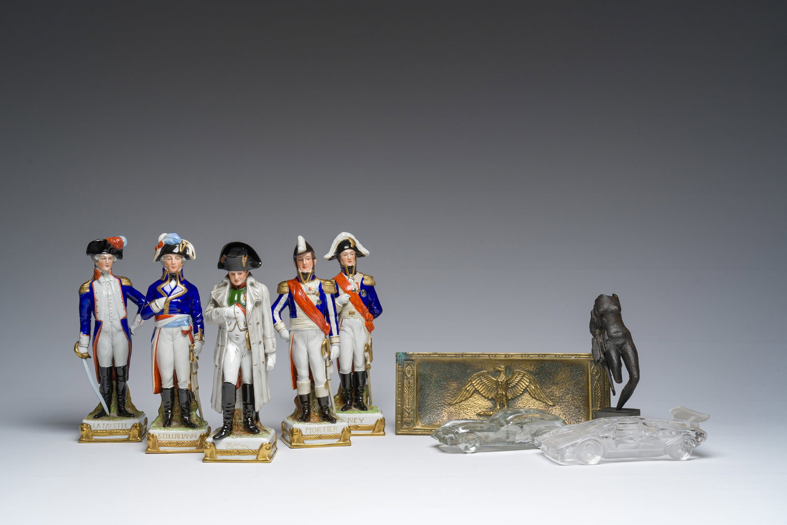 Five Saxon porcelain figures, a bronze 'eagle' pen holder, a sculpture and two glass sports cars,: Five Saxon porcelain figures, a bronze 'eagle' pen holder, a sculpture and two glass sports cars, 20th C. H 24 cm (the largest figure) H 18 cm (the smallest figure) L 18 - D 7,5 cm (the Lamborghini Co