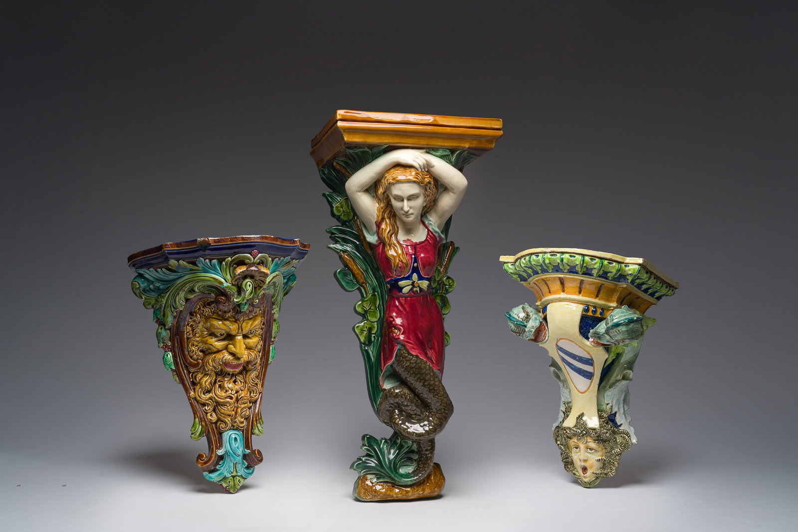 Three French polychrome maiolica consoles with a siren, a mascaron and a coat of arms, one with a (1 of 11)