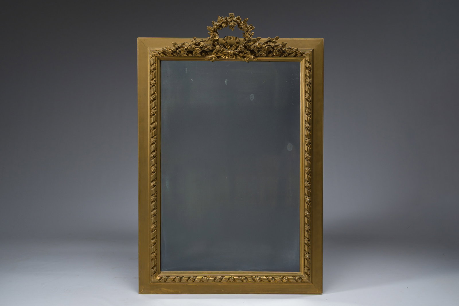 A rectangular French Louis XVI style gilt mirror crowned with a floral wreath, 20th C.: A rectangular French Louis XVI style gilt mirror crowned with a floral wreath, 20th C. Mirror: 88 x 58 cm Frame: 117,5 x 77,5 cm