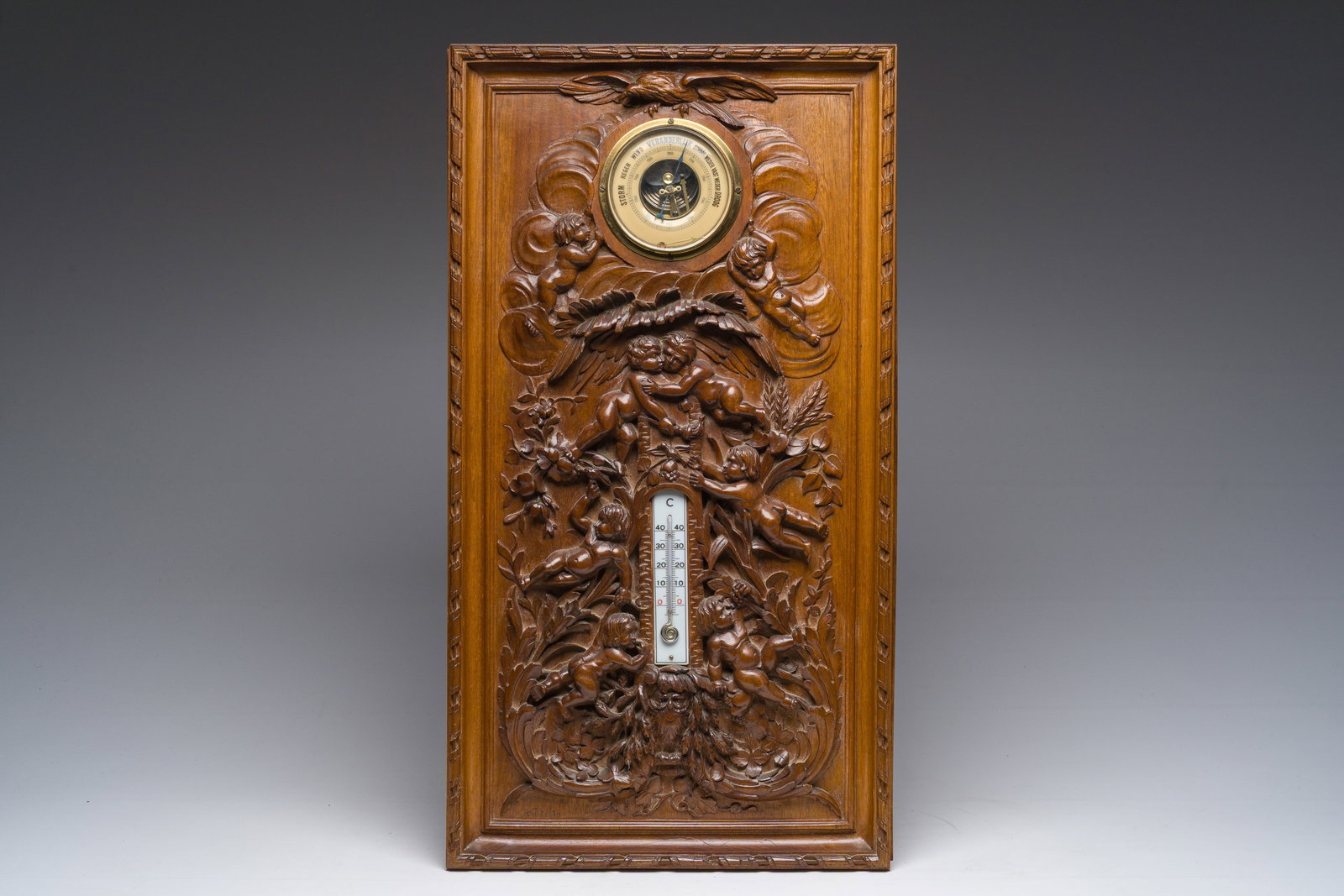 W. Thiel (19th/20th C.): A carved wooden weather station with thermometer and barometer with putti,: W. Thiel (19th/20th C.): A carved wooden weather station with thermometer and barometer with putti, an owl and an eagle 66 x 36 cm