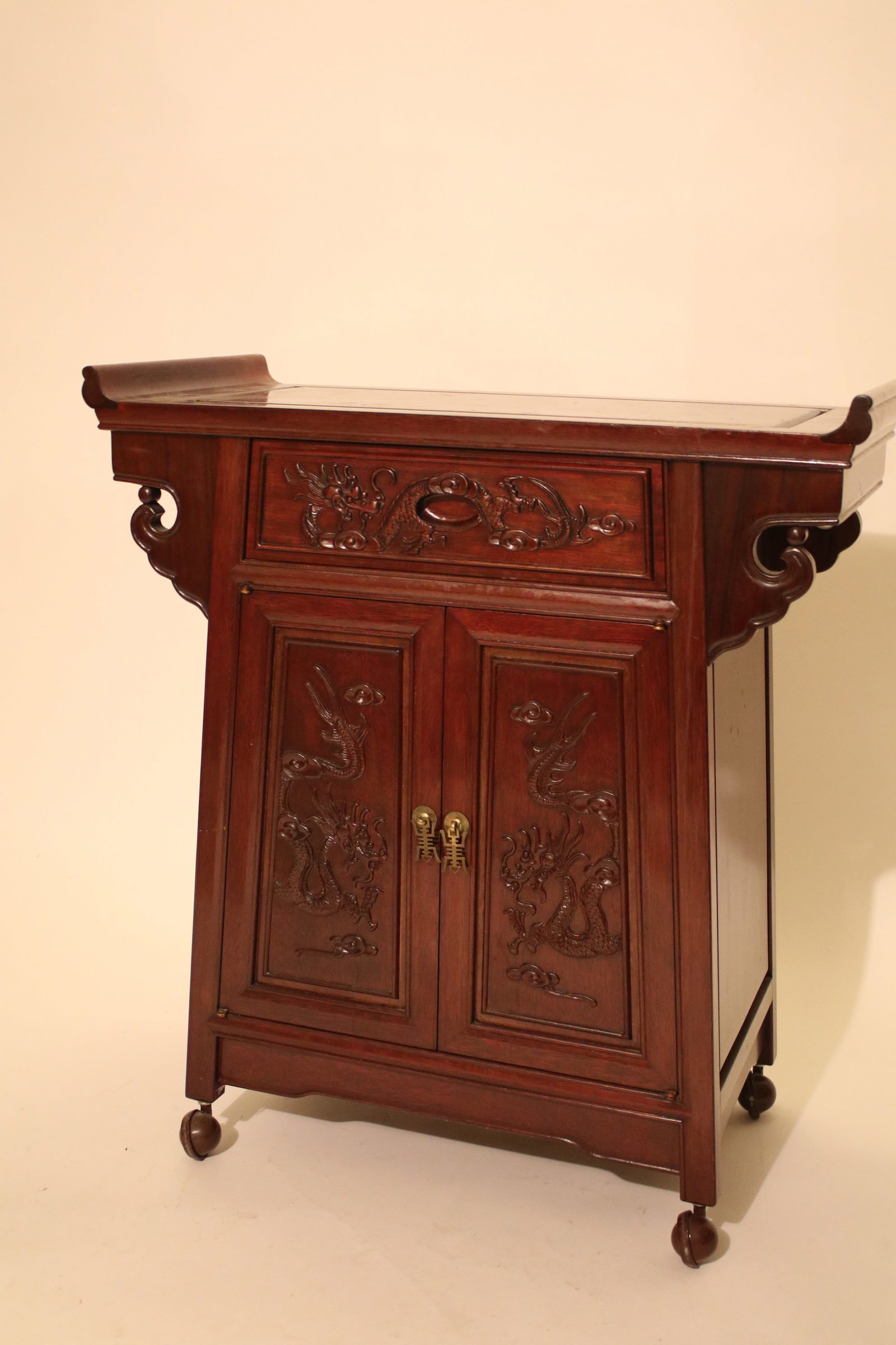 Chinese Altar Table with Caster Wheels: This Chinese altar table features a traditional silhouette with gently flared ends, carved apron details, and richly grained wood that gives it a warm, elegant presence. The front panel showcases intr