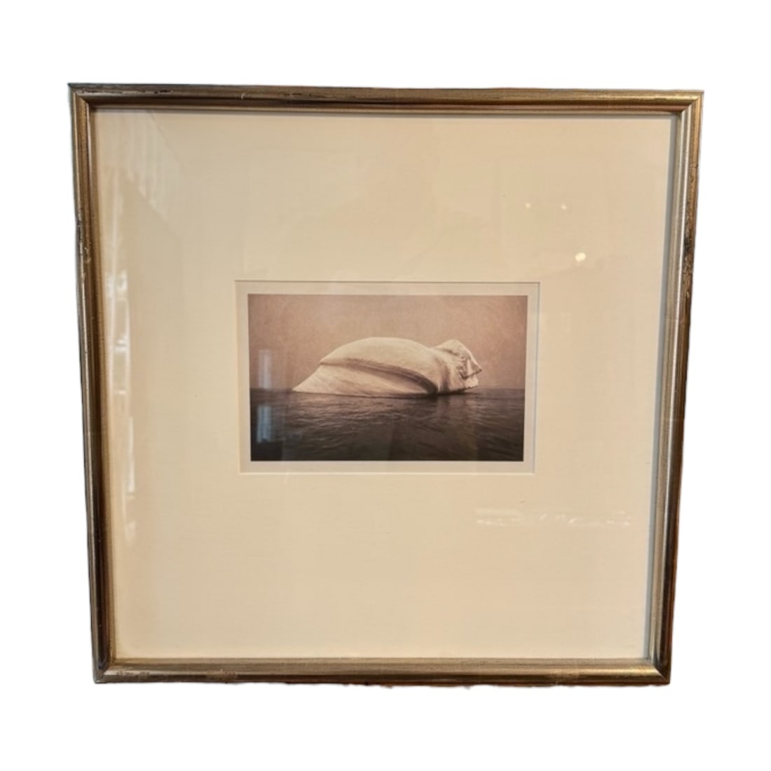 Surreal Iceberg Coastal Art Print: A striking surrealist-style coastal image featuring a monumental seashell rising from calm, reflective waters. The soft sepia tones and minimalist composition create a dreamlike atmosphere, blending n