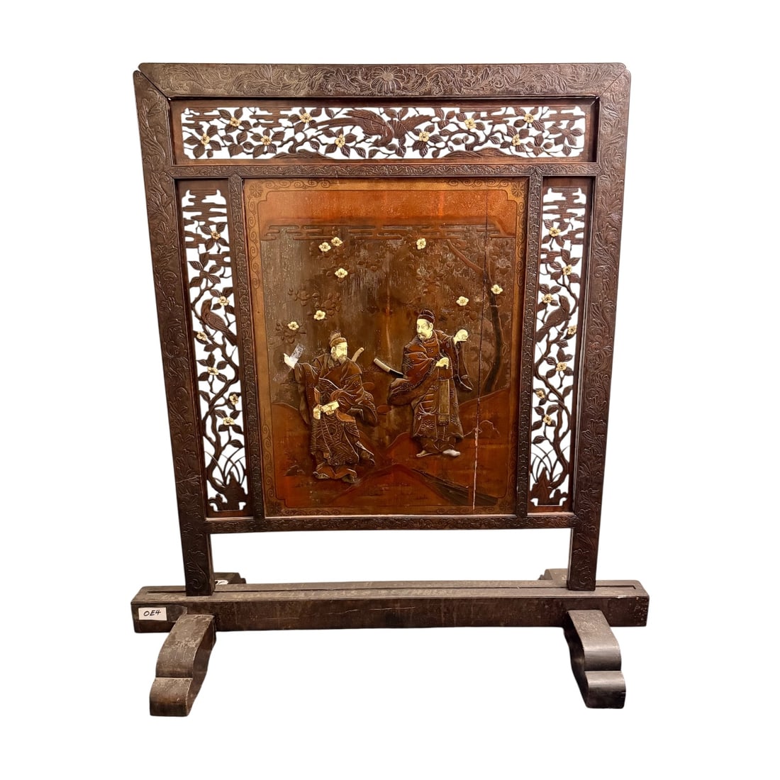 Japanese Carved Wooden Screen with Stand: Decorative Japanese wooden screen featuring carved floral and bird motifs surrounding a central relief panel depicting two robed figures beneath flowering branches. The piece is set within an ornate