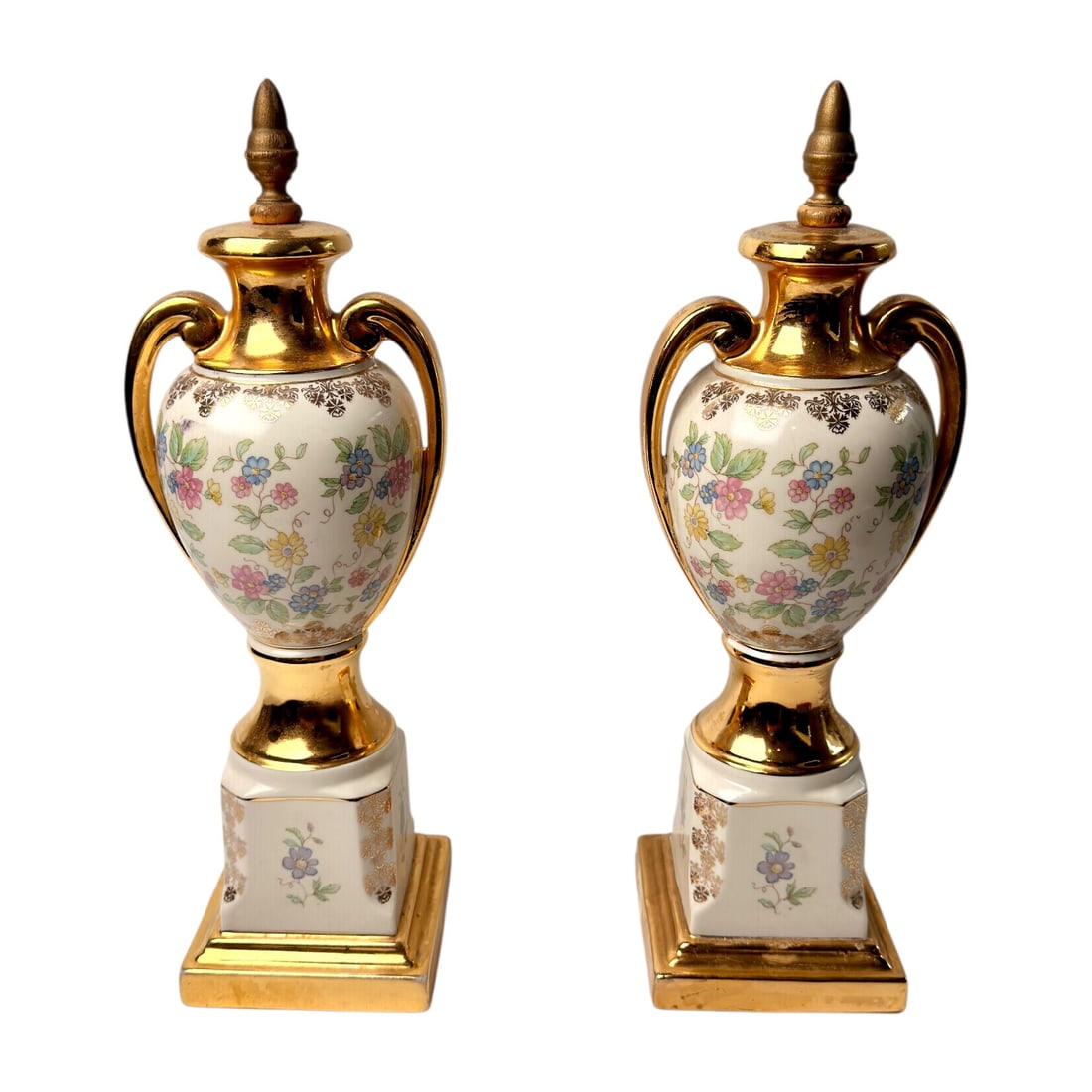 Pair of Floral Porcelain Urn Form Decorative Finials: Elegant pair of porcelain urn-form decorative finials featuring delicate hand-painted floral garlands accented with rich gilt decoration. Each urn is flanked by gracefully scrolled twin handles, toppe