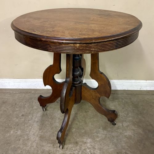 Antique Victorian-style Parlor or Side Table showcasing Decorative Edge Molding and Rests on a: Antique Victorian-style Parlor or Side Table showcasing Decorative Edge Molding and Rests on a central Turned Pedestal with a Scrollwork or Carved Tripod Base on Caster Wheels, likely dating from the