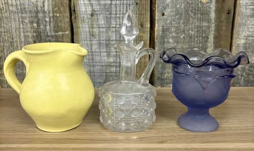 This lot features Three Distinct Collectible Items: Yellow Pottery Pitcher, a Clear Pressed Glass: This lot features Three Distinct Collectible Items: Yellow Pottery Pitcher, a Clear Pressed Glass Cruet, and a Blue Ruffled Glass Vase - 4-6"