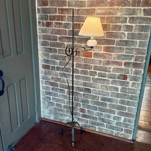 Wrought Iron Bridge Floor Lamp with Milk Glass Hobnail Accent 18"X57": This is a wrought iron bridge floor lamp featuring a slender central pole supported by a tripod base. The base is constructed from three scrolled strap-iron feet connected by a decorative cast-metal c