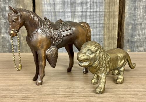 Two Vintage Brass - Cast Metal Animal Figurines, Saddled Horse and Lion: This lot features two vintage cast metal figurines consisting of a Western-style horse and a standing lion, frequently identified as mid-20th-century carnival or county fair prizes. The horse figurine