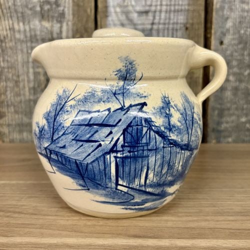 Paul Storie Pottery Stoneware Lidded Pitcher with Hand Painted Blue Barn Scene: This stoneware lidded pitcher was produced by the P.R. Storie Pottery Co. in Marshall, Texas. The vessel features a bulbous form with a pinched pouring spout, a single loop handle, and a matching fitt