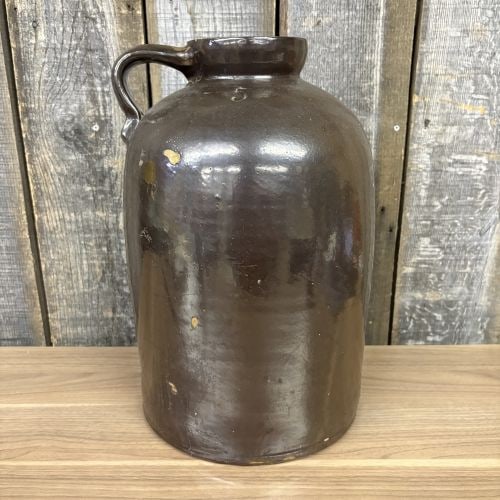 Five-Gallon Brown Slip Glazed Stoneware Jug: Large stoneware jug featuring a bulbous body tapering to a short, wide neck with a heavy, rounded rim. The vessel is finished in a dark brown Albany-type slip glaze with a glossy appearance, character