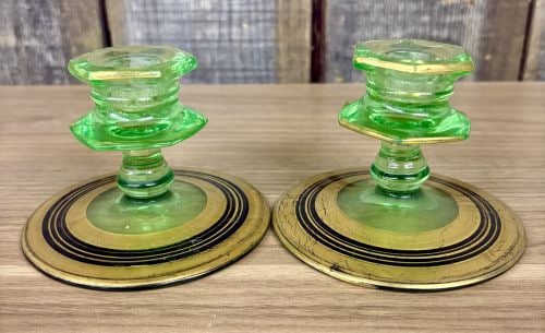 A Pair of Art Deco Green Uranium Glass Candlesticks with Gilt and Enamel Decoration: This pair of matching low-profile candlesticks is crafted from green uranium glass, a material characterized by its translucent light green color and fluorescence under ultraviolet light. The design i