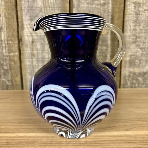 Cobalt Blue Art Glass Pitcher with Opaque White Festooned Decoration: A hand-blown art glass pitcher featuring a deep cobalt blue body. The vessel is decorated with opaque white combed or festooned patterns on the bulbous body and horizontal trailing around the flared r