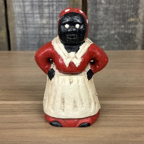 Vintage Aunt Jemima Style Still Bank: This still bank is modeled in the form of a woman with hands on hips, a design historically identified as an Aunt Jemima or Mammy figure. The object is a two-piece cast iron construction joined by a s