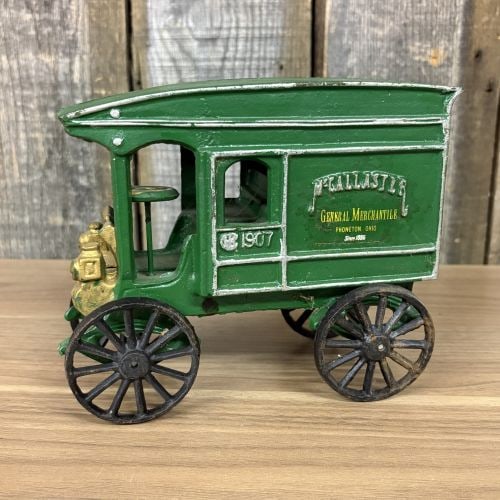 McCallaster General Mercantile 1907 Delivery Truck: This cast iron toy delivery truck is a commemorative or promotional piece modeled after a 1907 motor vehicle. The vehicle is finished in green paint with silver-painted trim and gold-painted accents o