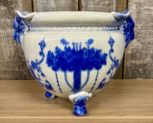 Large Flow Blue Earthenware Tripod Jardiniere with Ram Head Handles: Large ceramic tripod jardiniere or planter decorated in a flow blue style. The vessel features a bulbous earthenware body supported by three legs that terminate in cloven hoof feet. The piece is disti
