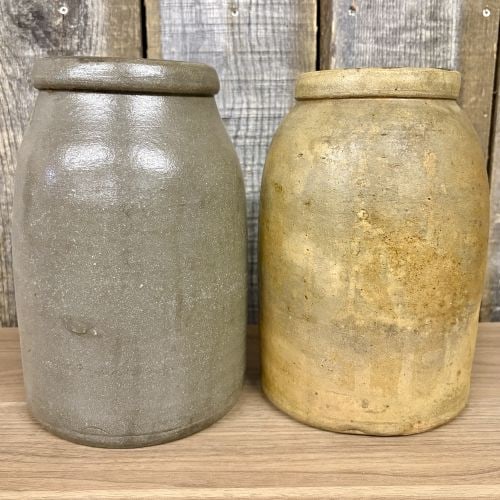 Two 19th-Century American Stoneware Storage Jars: Two American stoneware storage jars dating to the 19th century. These utilitarian vessels feature a cylindrical body tapering at the shoulder to a wide mouth with a thick, rounded rim. The gray jar is