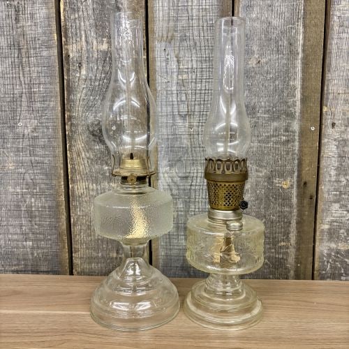 A Pair of American Vintage Pressed Glass Oil Lamps including Plume and Atwood: This lot features two American vintage pressed glass oil lamps. The first lamp (left) is constructed with a clear glass font characterized by a pebbled or crackle texture. It stands on a circular pede
