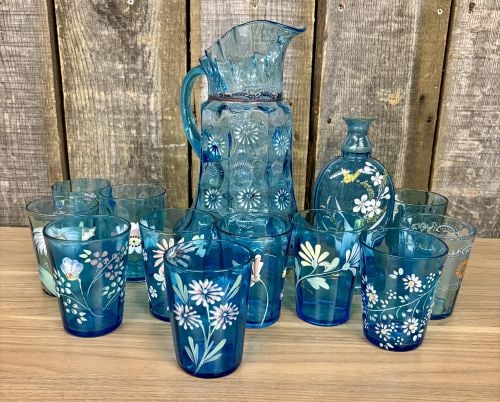 A 12-Piece Set of Victorian-Style Enameled Blue Art Glass Tableware Attributed to Fenton or: This 12-piece set of transparent electric blue art glass is characteristic of Victorian-era production, attributed to American glassmakers such as Fenton or Northwood. The set consists of a pitcher, a