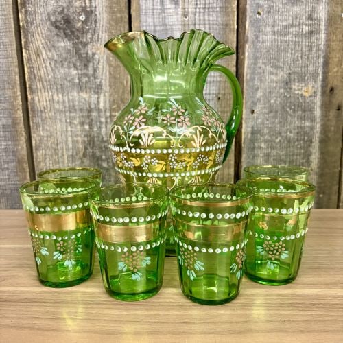 Seven-Piece Emerald Green Enameled Glass Beverage Set: This seven-piece set comprises a pitcher and matching tumblers crafted from transparent emerald green glass. The pitcher is mold-blown and features a hand-finished ruffled rim with an applied solid gr