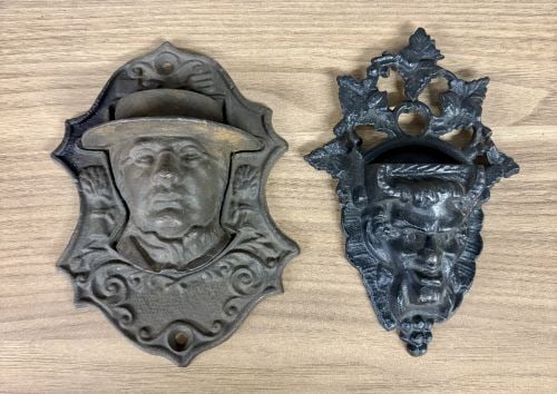 Two Victorian Cast Iron Wall-Mounted Match Pockets including Horace Greeley Depiction: A lot consisting of two decorative cast iron wall-mounted match holders. The first holder is shield-shaped and features a relief-cast portrait of a man in a wide-brimmed hat, identified by historical 