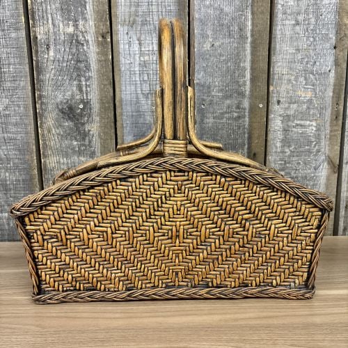 Mid-Century Modern Woven Rattan and Reed Magazine Rack: A large magazine rack or catch-all basket constructed with a sturdy rattan pole frame and intricate split reed weaving. The piece features a prominent double-arched handle secured to the sides with ra
