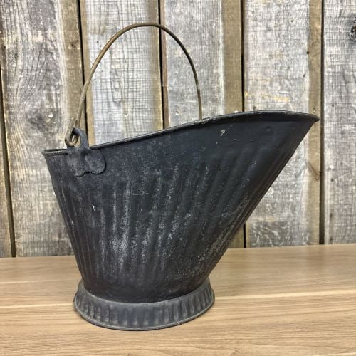 Vintage Painted Metal Helmet Coal Scuttle with Brass Handles: A vintage coal scuttle of traditional helmet form, constructed from black-painted sheet metal. The body features vertical fluted ribbing that extends around the circumference and onto the flared pedes