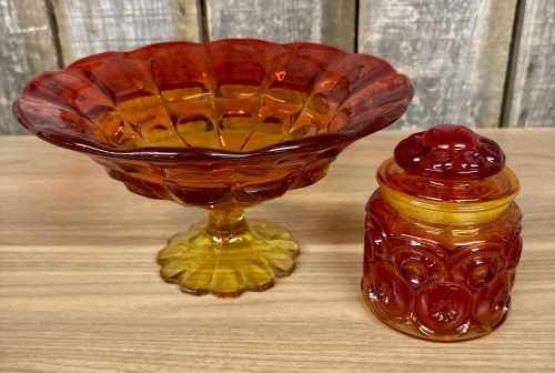 Two Pieces of Vintage Amberina Glass including a Large Pedestal Compote and a Lidded Jar: This lot comprises two pieces of mid-century American pressed glass in the Amberina colorway, which features a gradient transition from amber-yellow at the base to ruby red at the rim. The first item 