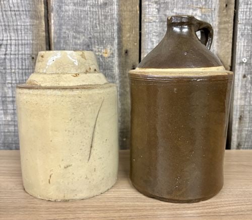Two Antique Cylindrical Stoneware Vessels: This lot consists of two antique stoneware vessels. The first is a cylindrical jar with a stepped, tapering shoulder and a wide mouth, finished in a light cream-toned glaze with iron spotting. An inci