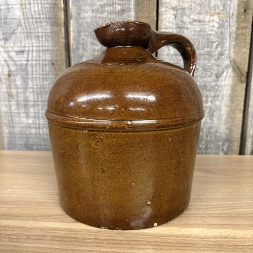 Antique Brown Slip Glazed Stoneware Jug with Pancake Spout: This antique stoneware jug is a classic example of 19th-century American utilitarian pottery, featuring a cylindrical body that tapers to a rounded shoulder. It is equipped with a single applied strap